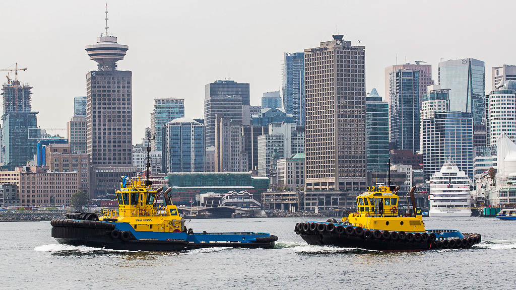 Two harbour tugs crossing Burrard Inlet in front of the Vancouver skyline